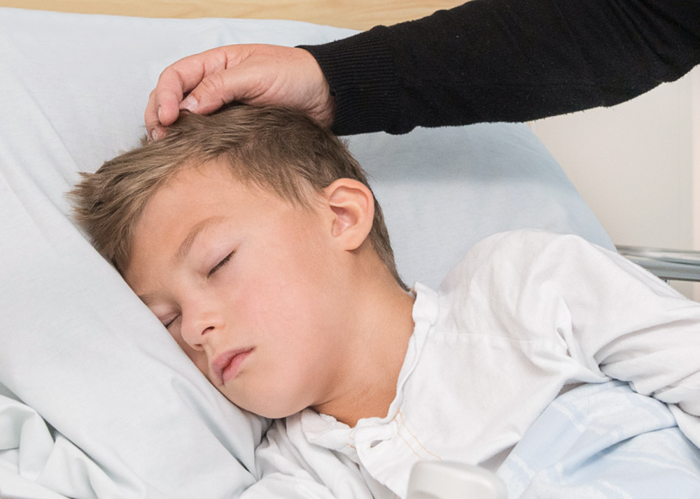 Boy sleeping in bed. His mother pats him on the head.