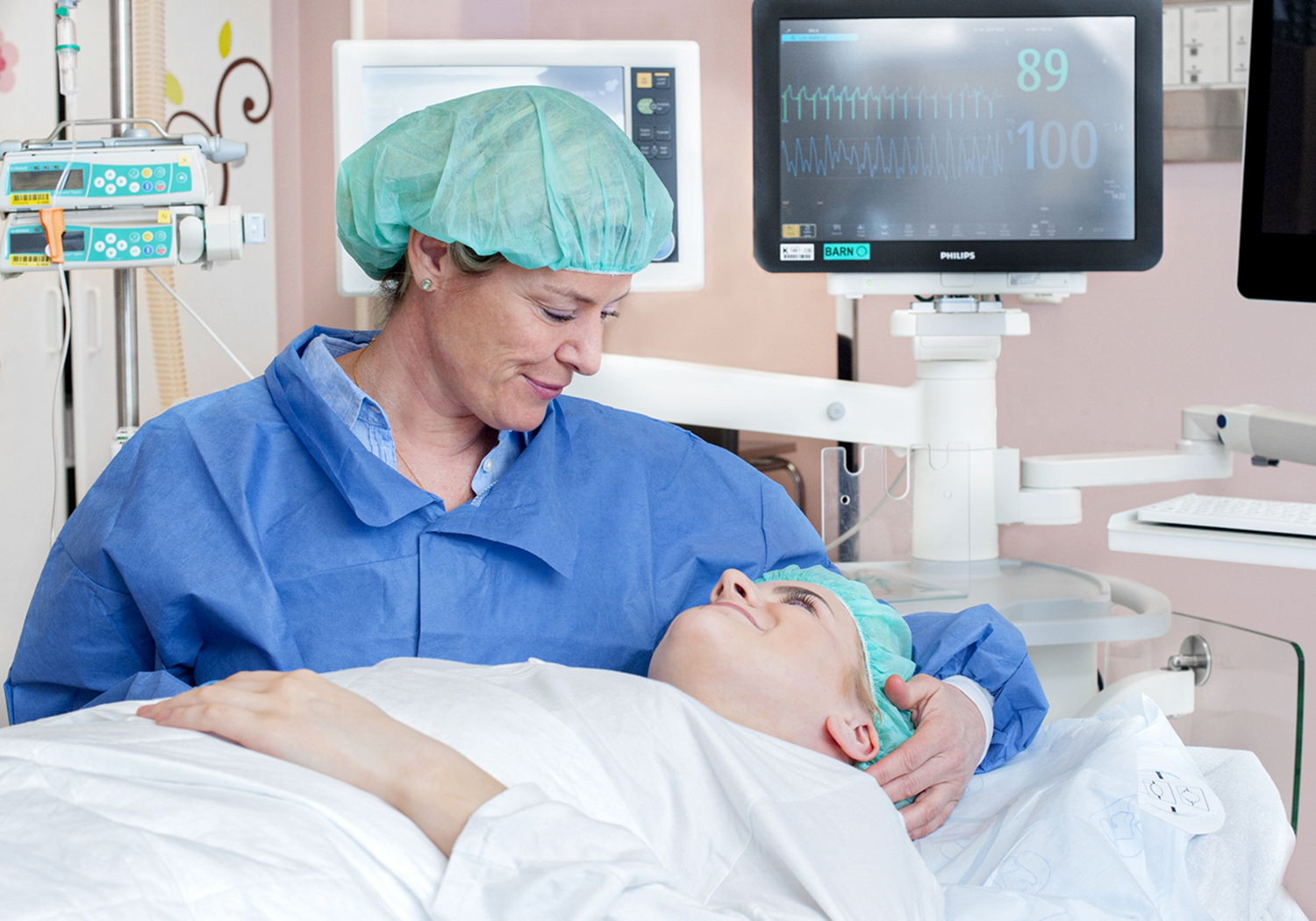 Teenage girl lying on an operating table. Her mother is beside the bed wearing scrubs and scrub cap.