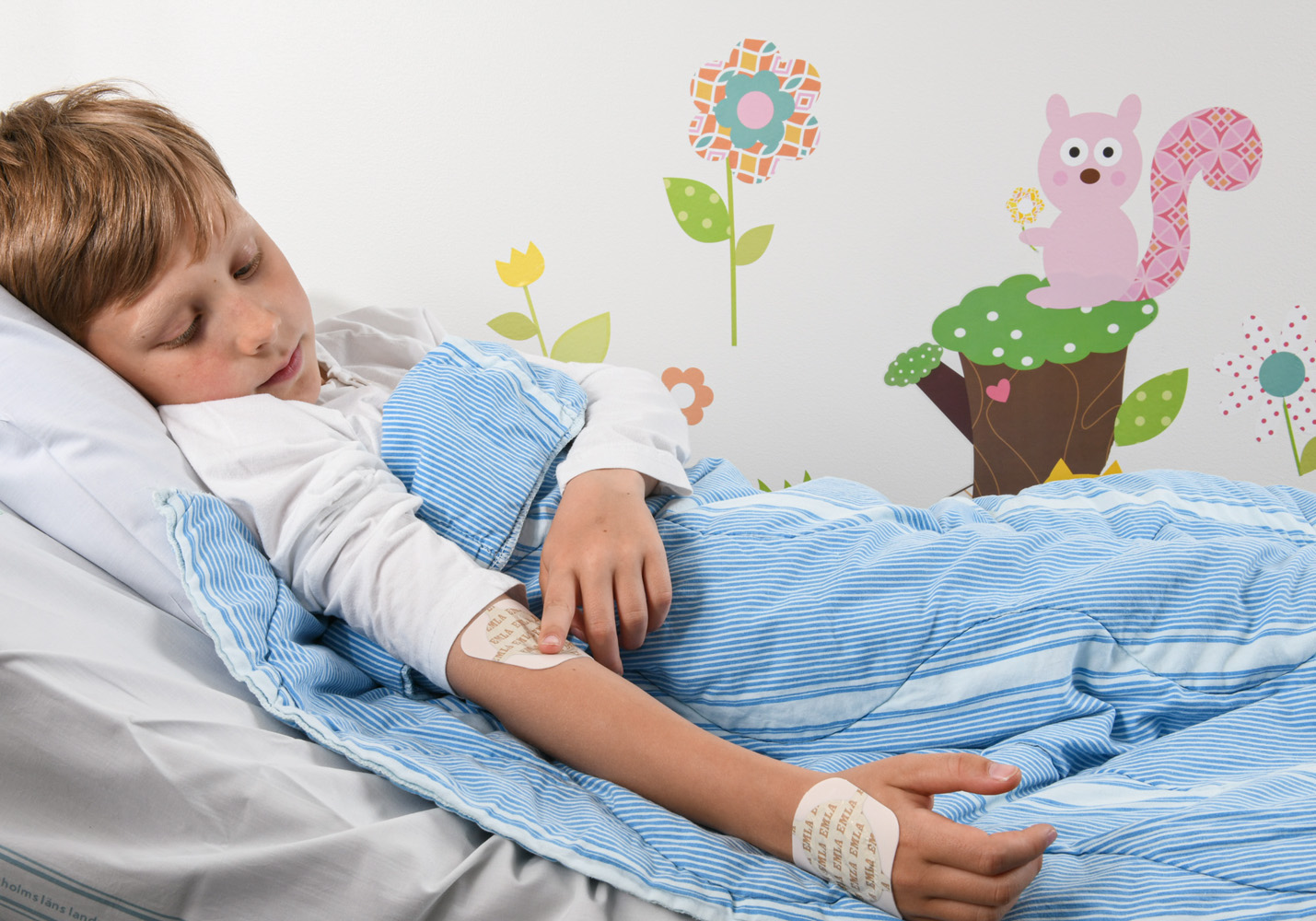 Frank lying in a hospital bed with big, square plasters on him – one in the crook of his arm, one on his hand.