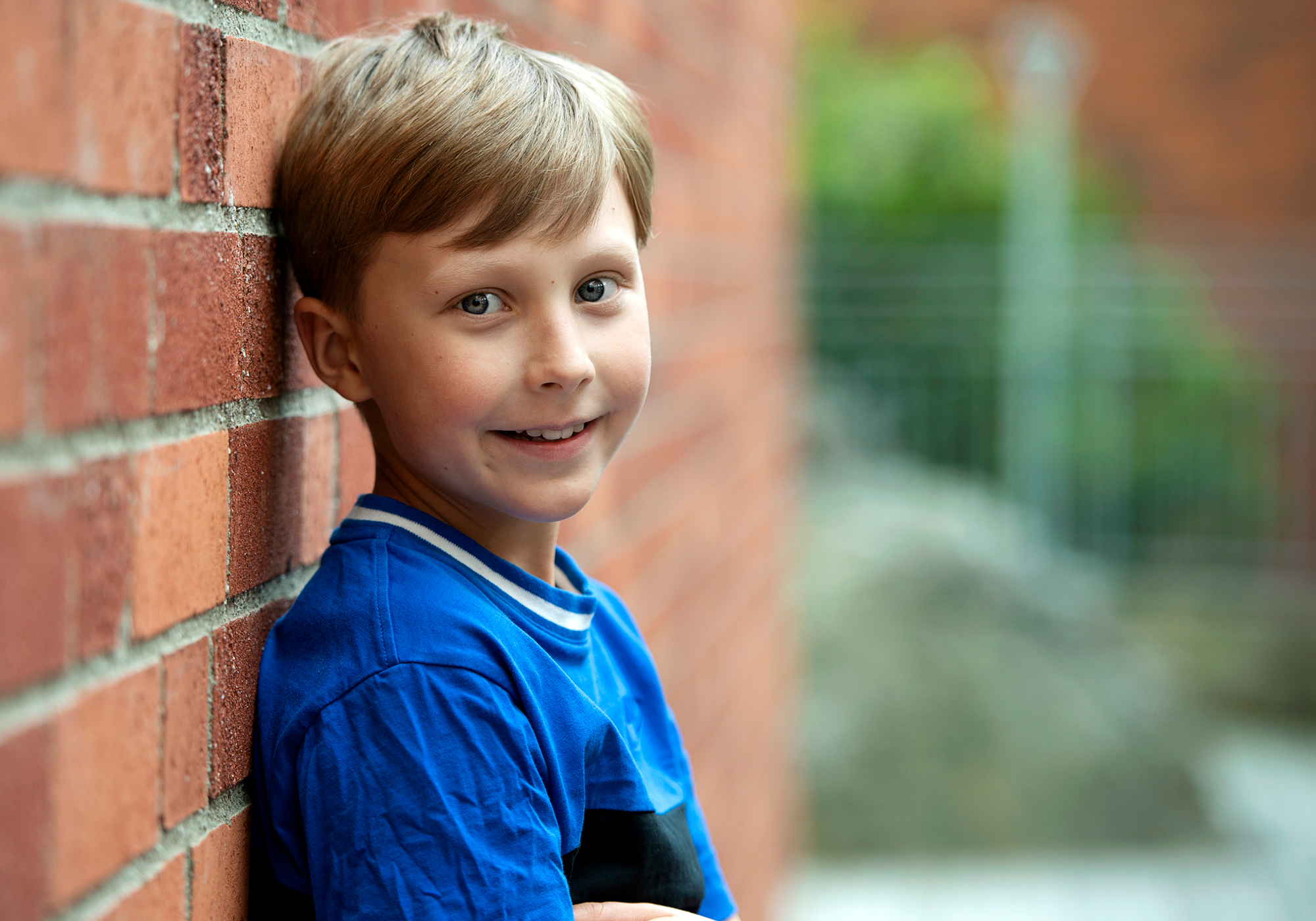 Frank, aged 9, leaning against a brick wall and looking happy.