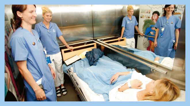 Ronja and two nurses in the elevator on their way to surgery. Ronja is lying in her bed.