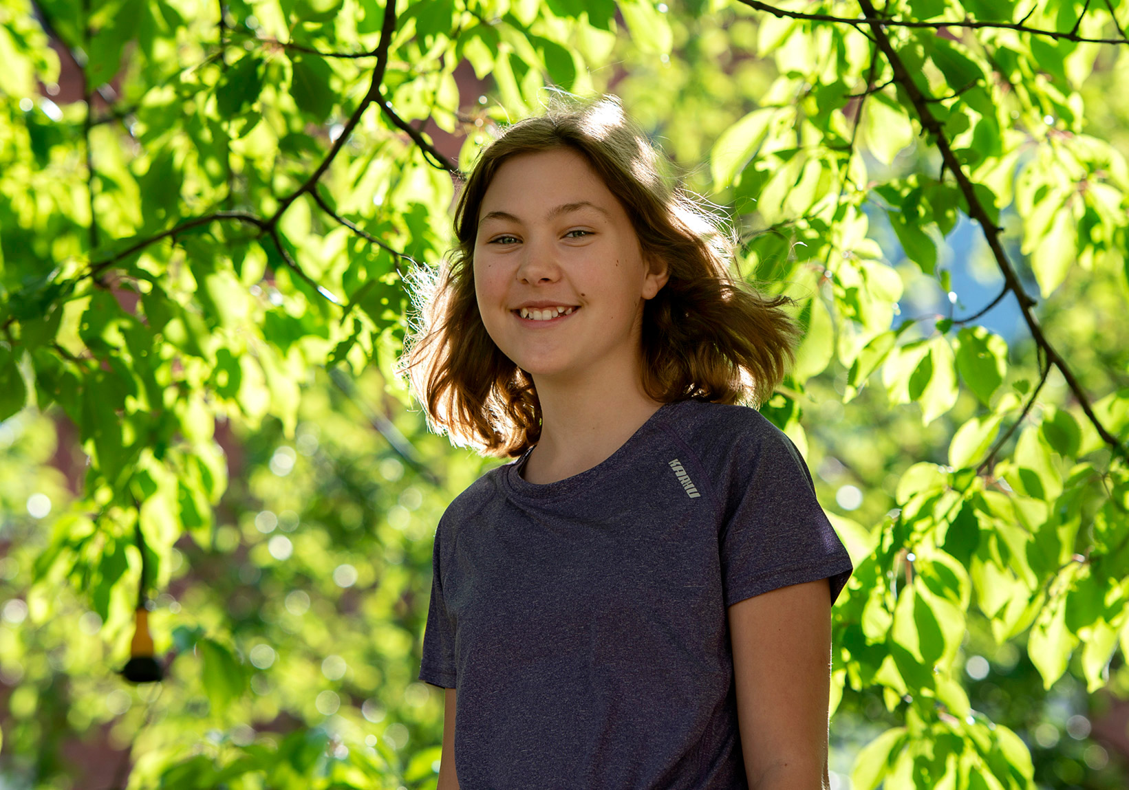 Mathilda, 14, smiles at us. Green trees in the background.