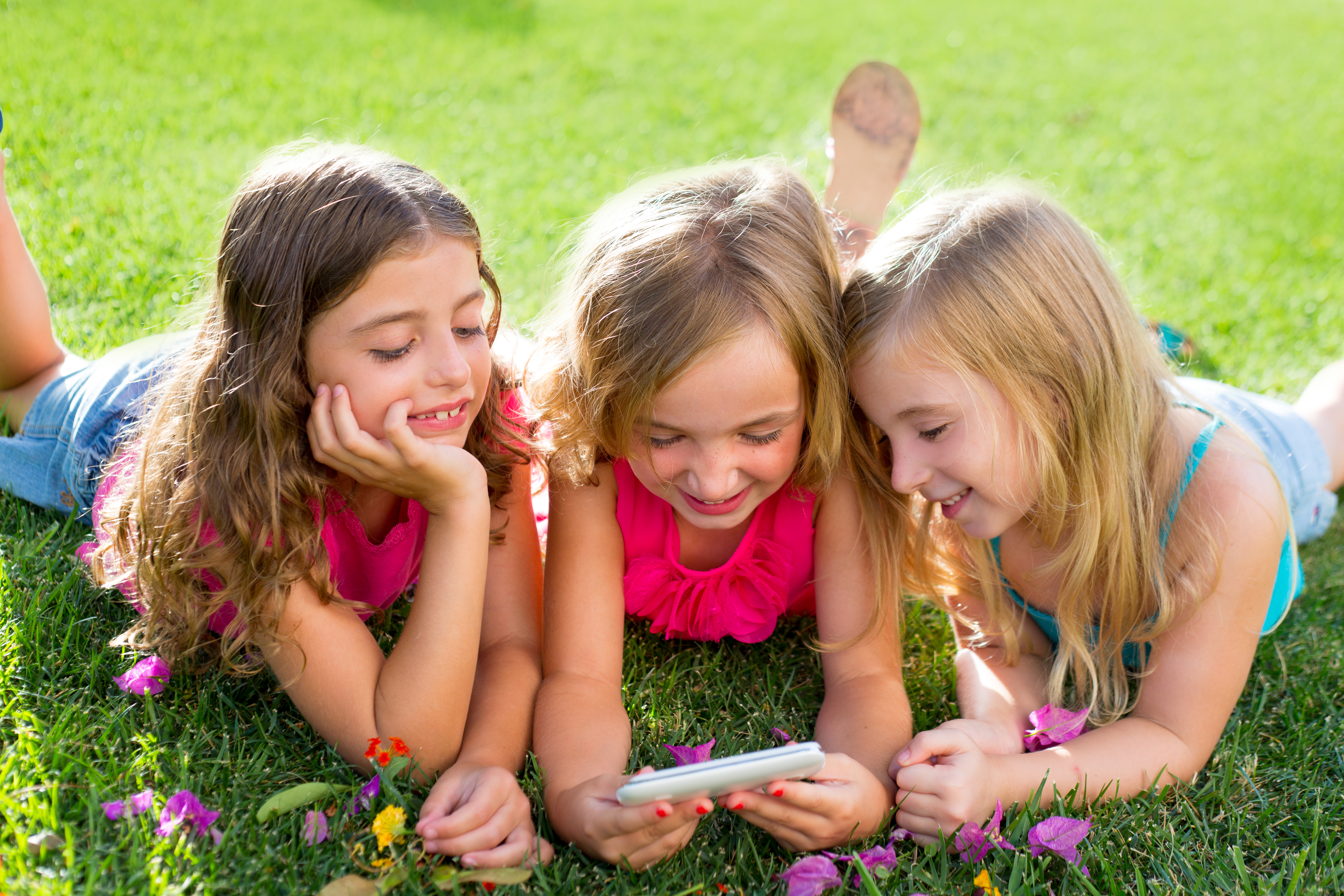 Three girls are lying on the grass and looking at a mobile phone.