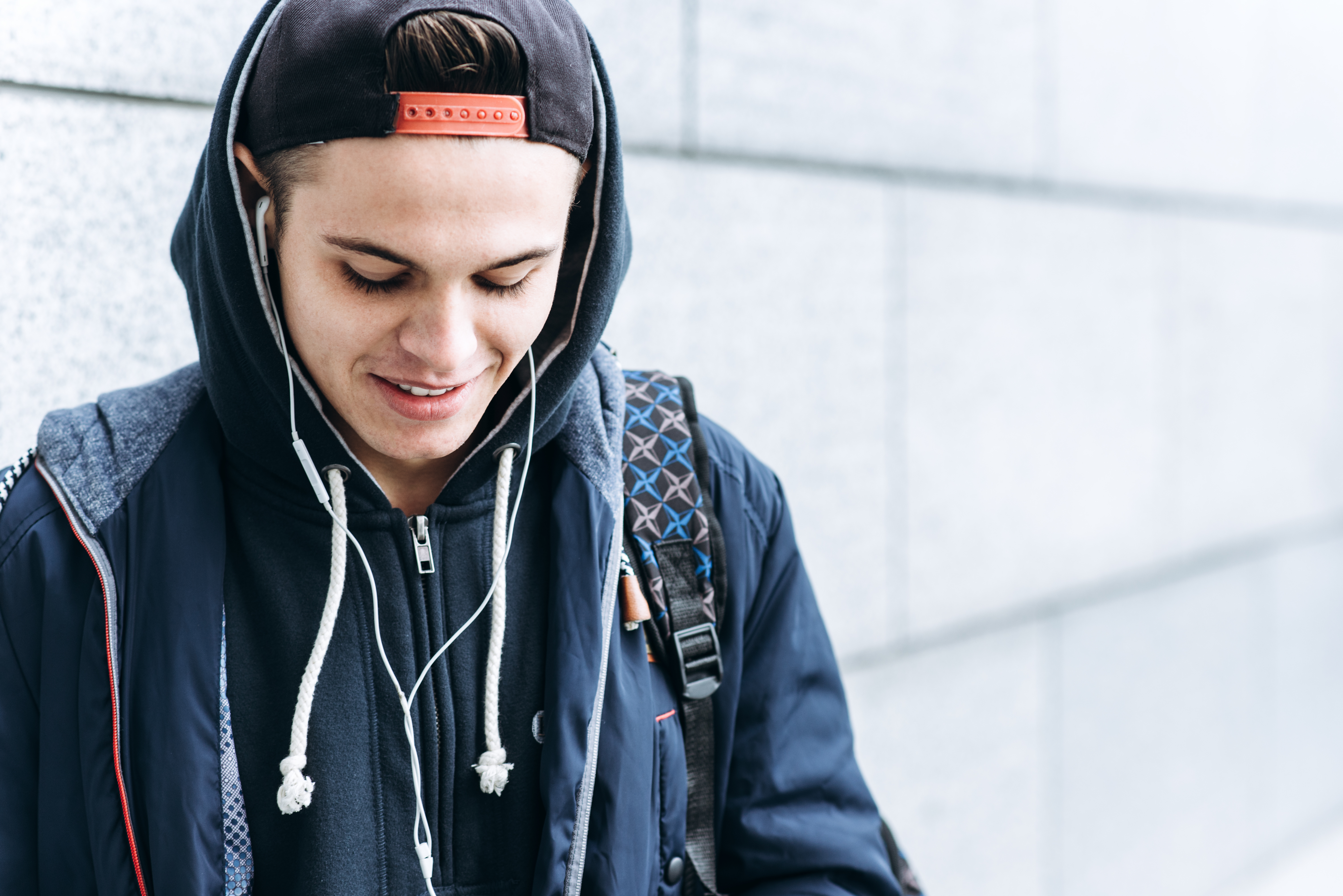 Teenage boy in black cap and hoodie looks down at the ground.
