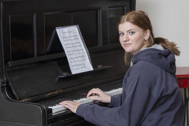 Teenage girl in a black hoodie playing piano.