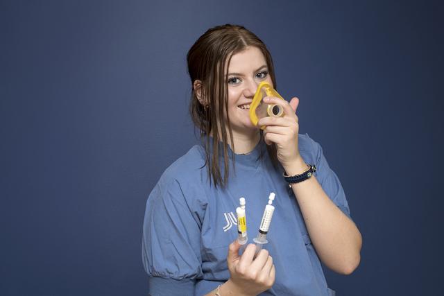 Teenage girl in scrubs holding syringes in one hand and an anaesthestic mask in the other.