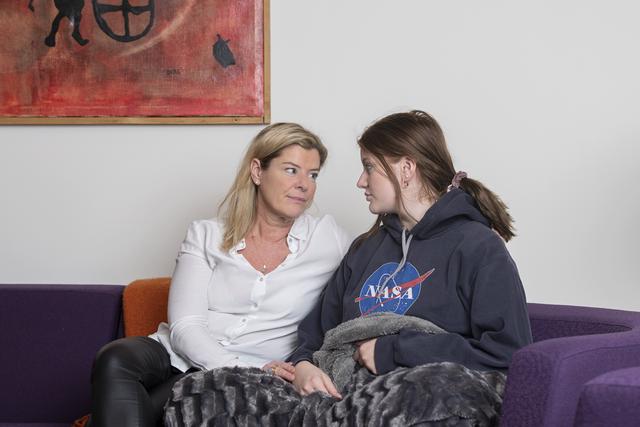 Teenage girl and her mother in a sofa. They are looking at each other.