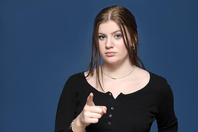 Teenage girl in black sweater pointing to the camera.