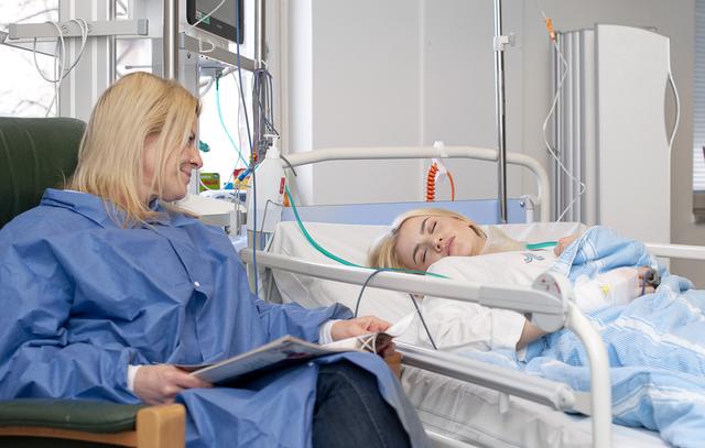 Operated girl sleeping in her bed in the recovery unit. Her mother is sitting beside the bed.