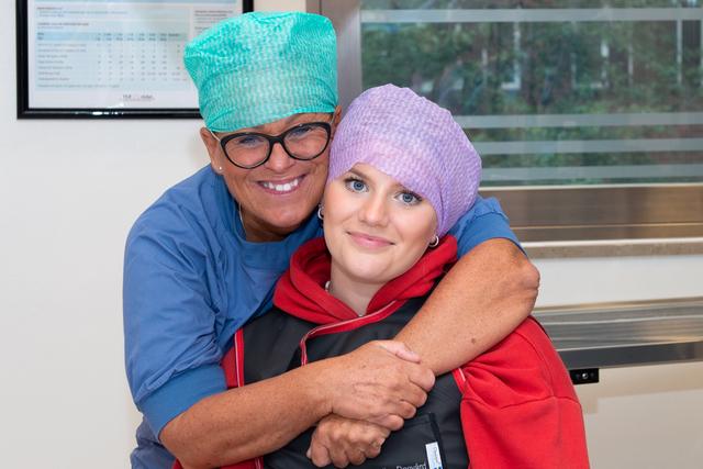 Teenage girl in a purple scrub hat getting a hug from a nurse anaesthestist.
