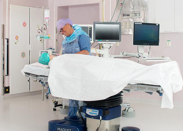 A teenage girl on a operating table in the operating room. A nurse staying beside the table.