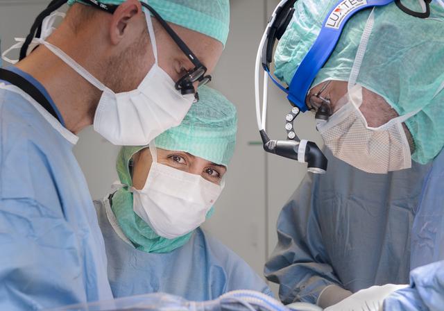 Three surgeons operating. One of them looking into the camera.